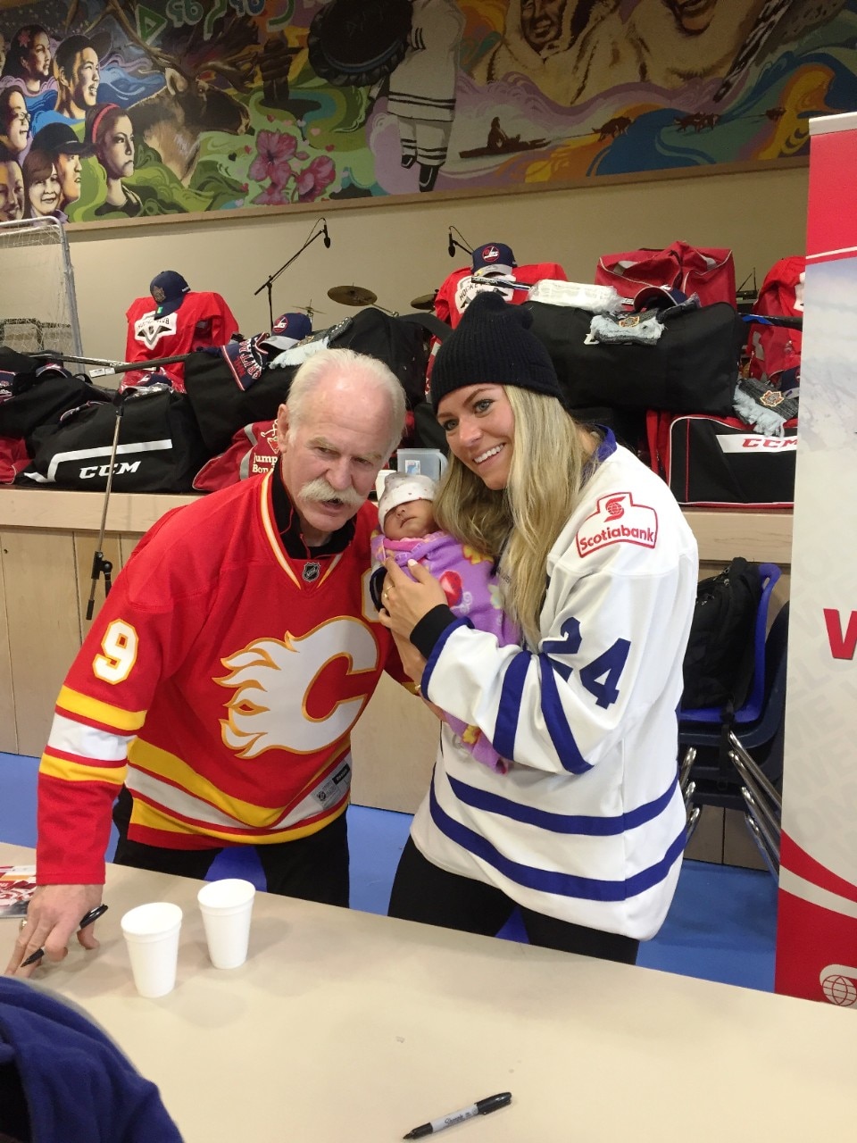 A very young fan poses for a picture with Lanny, Natalie and lots of new donated hockey equipment in the background, during the Project North event celebration in Gjoa Haven.