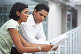 A man and woman sharing a newspaper.
