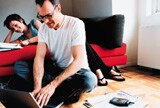 Couple at home reading and working on laptop