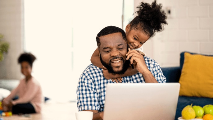 Father looking at a laptop with his child hanging around his shoulders