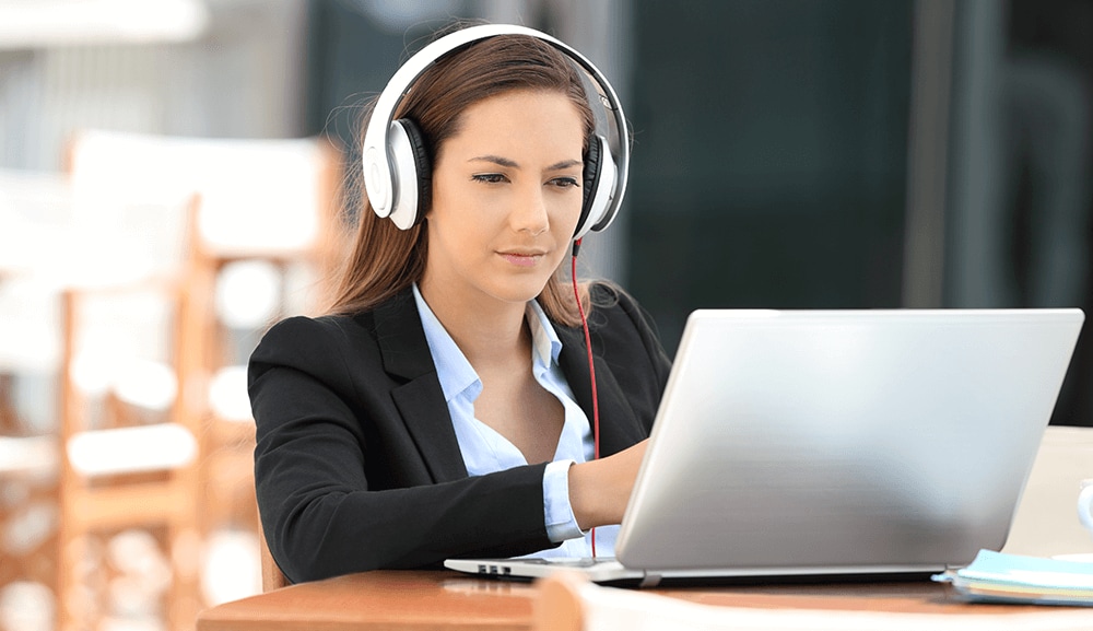 Women working at desk on her laptop with headphones.