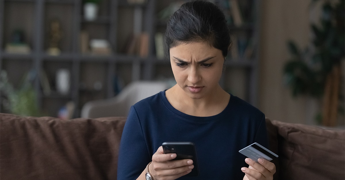 Woman holding down credit card and looking down with concern at cell phone