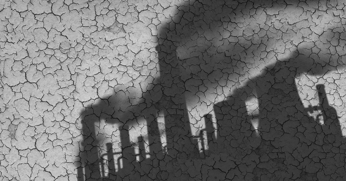 Shadow of industrial smokestacks shown on cracked ground