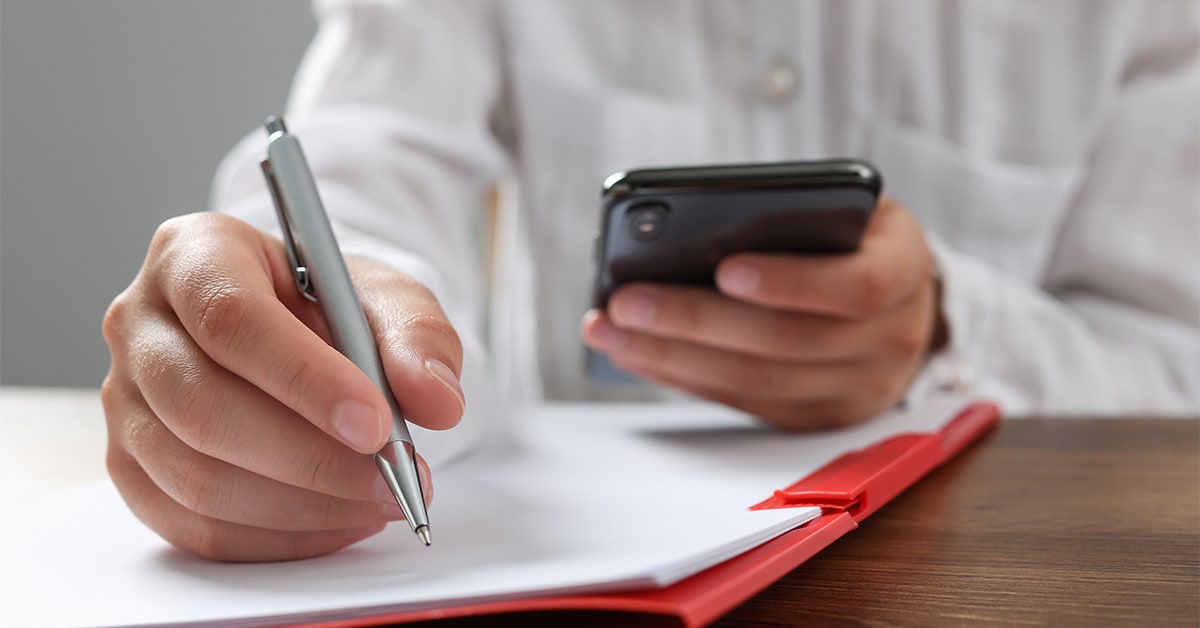 Personne tenant un téléphone portable et écrivant sur du papier