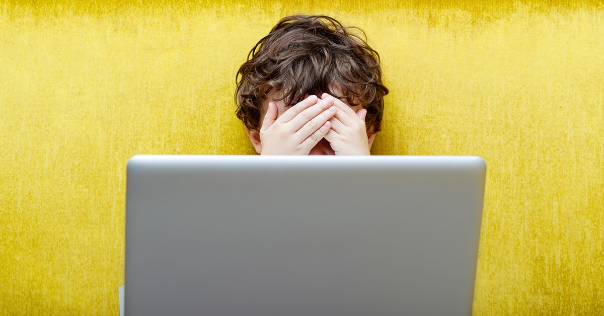 Niño con computadora ocultando sus ojos