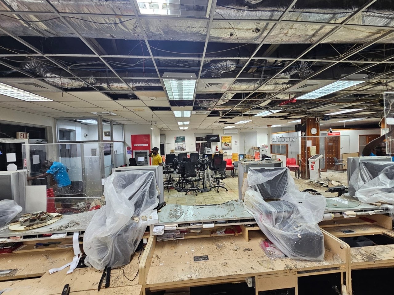 Second angle of Bank branch interior with roof panels missing and computers covered in plastic bags
