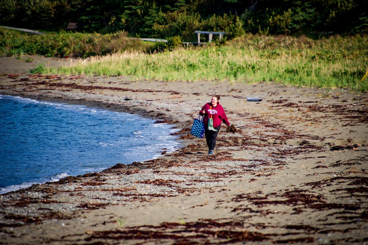 Woman walking along beach with seaweed washed up