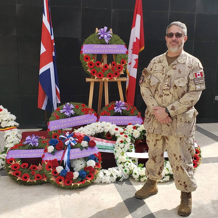 Luis standing in uniform in front of wreaths for Remembrance Day